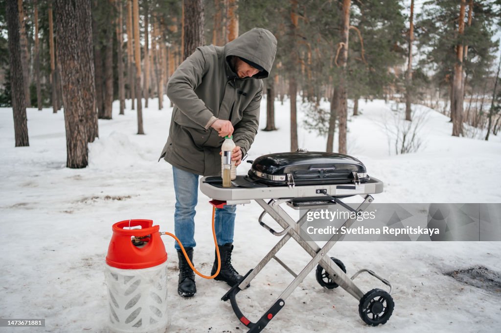 Man fries pancakes on a gas grill in a snowy forest in the spring picnic