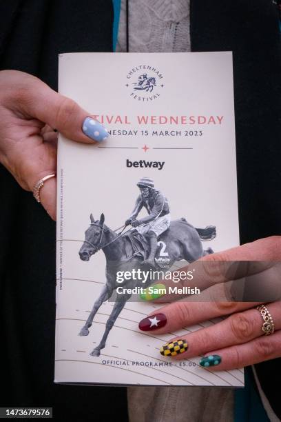 Lady holds a festival program with painted nails in the colours of Irish Jockeys including Honeysuckle, a thoroughbred racehorse during day two of...