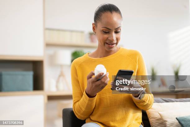 femme tenant un flacon de pilules et un mobile - comprimés en flacon photos et images de collection