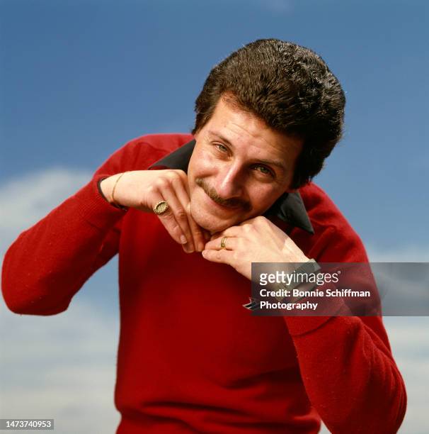 Musician Pete Best poses with his chin resting on the backs of his hands like a cheub while wearing a red sweater in Los Angeles in 1982.