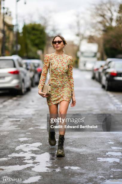 Emy Venturini wears vintage sunglasses, a yellow / green / red floral pattern print mini dress with long sleeves from Ganni, a beige bag with stripes...