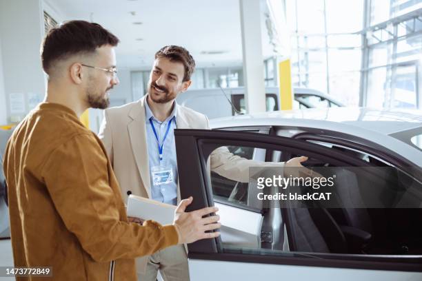 salesman in car showroom showing a new model of the car to the customer - customer test drive stock pictures, royalty-free photos & images