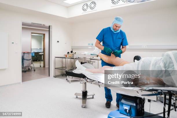 surgeon wrapping elastic bandage on patient knee after surgery in operation room - elastic bandage stockfoto's en -beelden