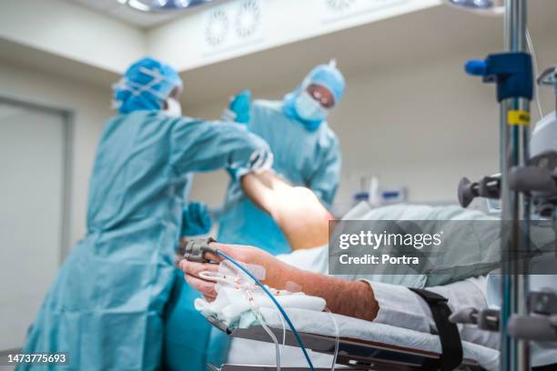 patient electronic pulse clip and iv drop undergoing surgery in operation room - man lying on operating table stock pictures, royalty-free photos & images