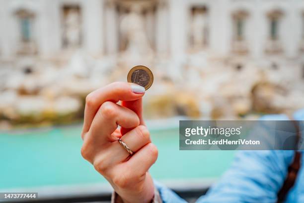 una mujer sosteniendo una moneda frente a la fontana de trevi - fontana de trevi fotografías e imágenes de stock