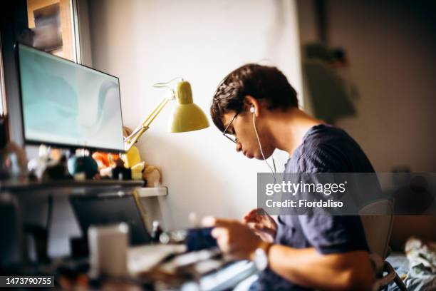 a teenager bespectacled guy sitting at his desk at home, studying programming, watching a video on a computer. home distance learning video conference. child with cerebral palsy - disabilitycollection ストックフォトと画像