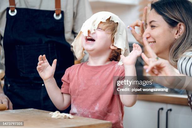 boy having fun kneading dough while father and mother cooking in home kitchen, family relationship concept - família de verdade imagens e fotografias de stock
