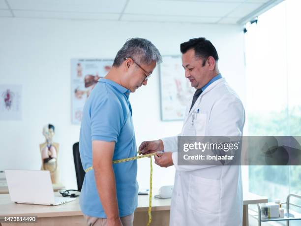 doctor measures patient's abdomen with measuring tape - fat asian man stockfoto's en -beelden