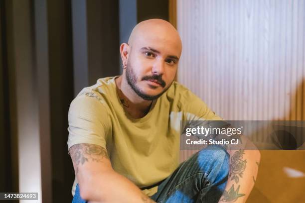 portrait young man sitting on sofa and looking at camera - bald man stockfoto's en -beelden