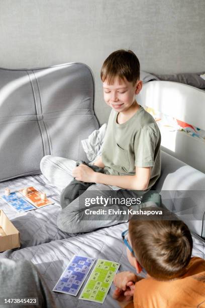 two boys are playing the board game loto lying on the couch on the day off - bingo card stock-fotos und bilder