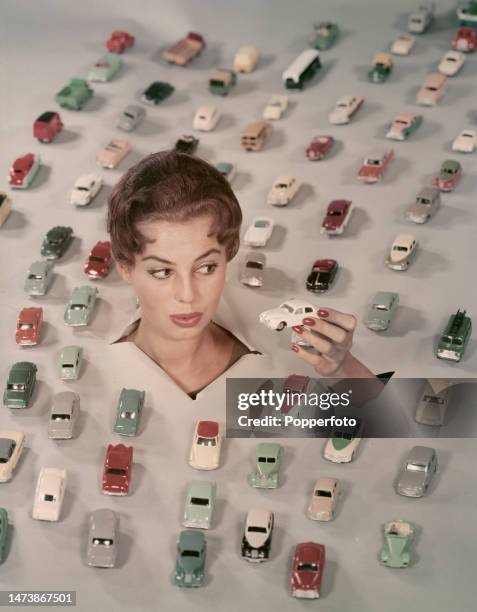 Posed studio portrait of a woman with a selection of 'matchbox' style die-cast toy models of mainly British built cars, she holds one car in her...