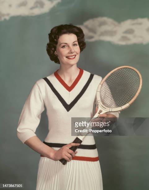 Posed studio portrait of a woman wearing a white knitted V necked sports jumper with red and blue striped detail and integrated pleated skirt, she...