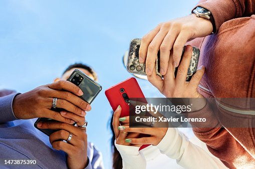 Low angle view of three young people using mobile phones outdoors Low angle view of three young people using mobile phones outdoors