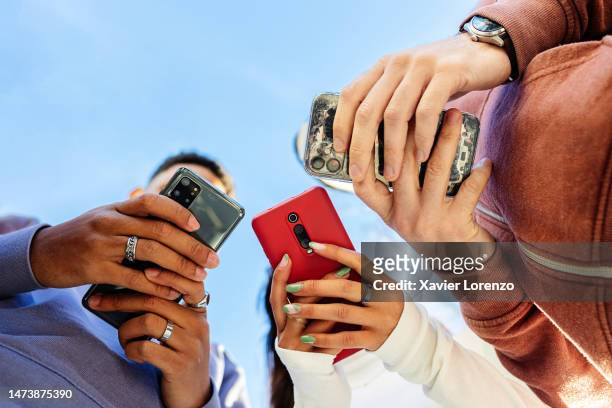 low angle view of three young people using mobile phones outdoors - social media stock pictures, royalty-free photos & images