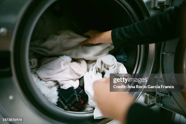 woman hands putting her dirty clothes in the washing machine in a laundromat - lavadora fotografías e imágenes de stock