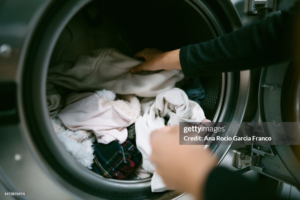 Woman hands putting her dirty clothes in the washing machine in a laundromat
