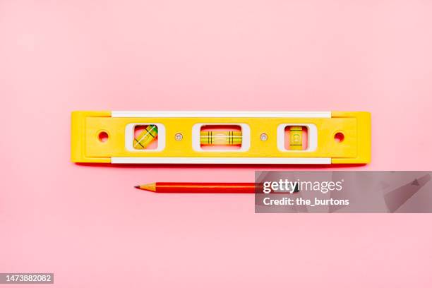 high angle view of yellow spirit level and pencil on pink background - waterpas stockfoto's en -beelden