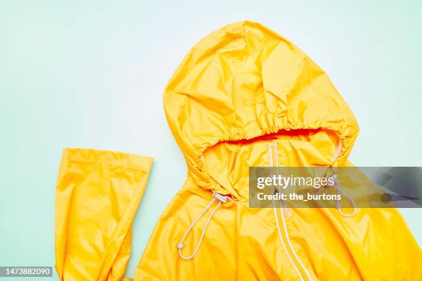 orange raincoat with hood on turquoise colored background - レインコート ストックフォトと画像