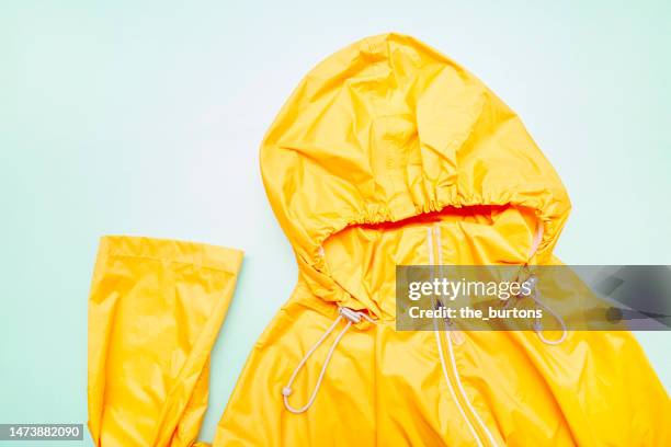 orange raincoat with hood on turquoise colored background - raincoat stock pictures, royalty-free photos & images