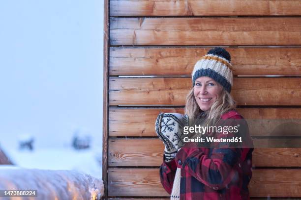 smiling mature woman wearing knit hat standing in balcony - headwear stockfoto's en -beelden