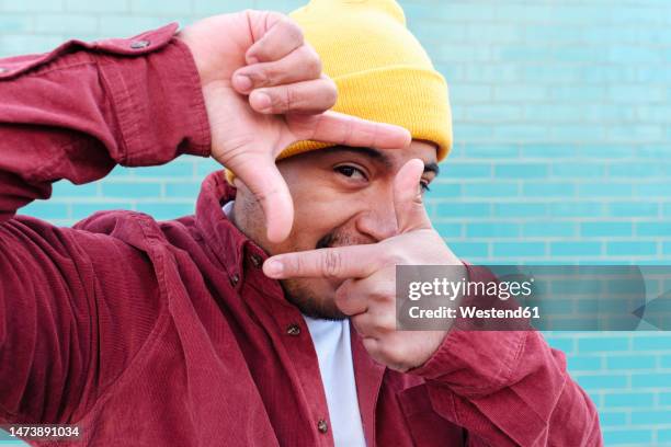 man looking through finger frame in front of turquoise brick wall - facial expression stock pictures, royalty-free photos & images