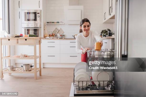 woman arranging crockery in dishwasher at home - dishwasher stockfoto's en -beelden