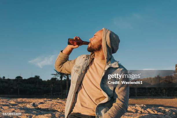 man drinking beer at sunset under sky - bottle beer foto e immagini stock