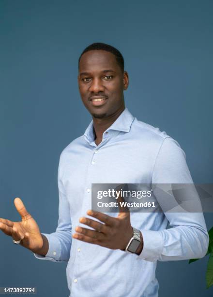 smiling businessman gesturing against blue background - chances stockfoto's en -beelden