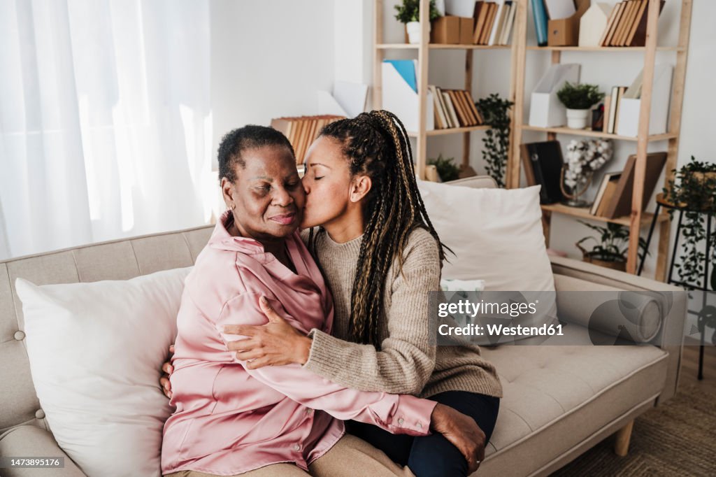 Daughter kissing mother sitting on sofa at home