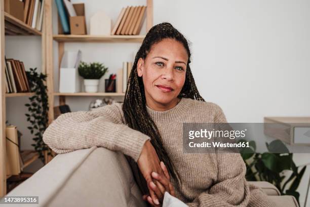 smiling woman sitting on sofa at home - mujer 50 años fotografías e imágenes de stock
