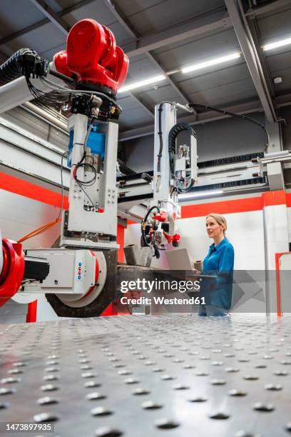 mature engineer examining robots with laptop in factory - braço robotizado imagens e fotografias de stock