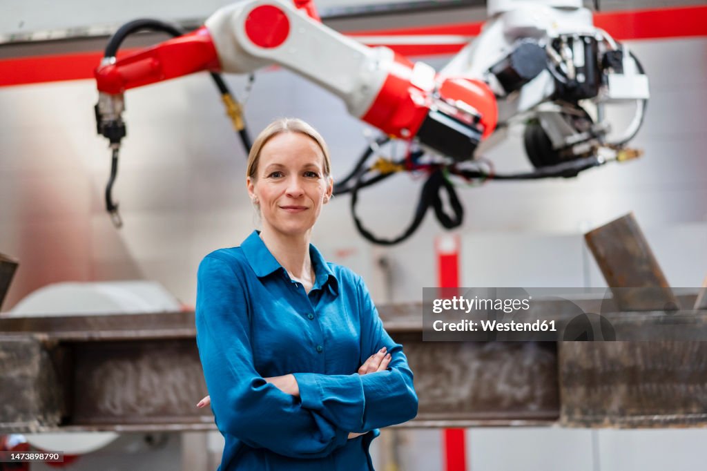 Confident mature technician with arms crossed at factory