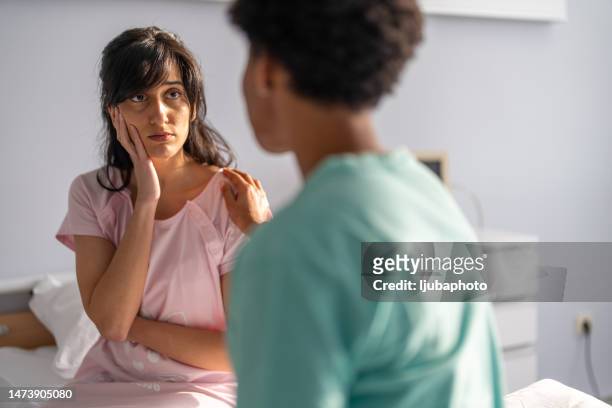 sad female patient looking at doctor in hospital - mid adult patient stock pictures, royalty-free photos & images