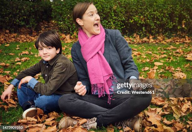 excited woman sitting cross-legged by boy at park - nephew stock pictures, royalty-free photos & images