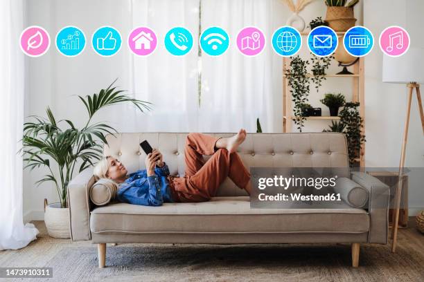 woman lying on sofa and using mobile phone app at home - smartphone hologram stockfoto's en -beelden