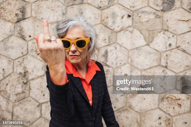 mature businesswoman gesturing in front of wall - doigt dhonneur fotografías e imágenes de stock