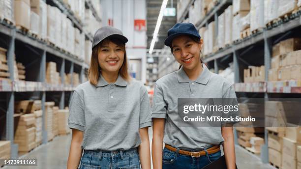 group of young asian women worker looking at camera and holding digital tablet stand in retail warehouse. business warehouse online. - t shirt uniform stock pictures, royalty-free photos & images