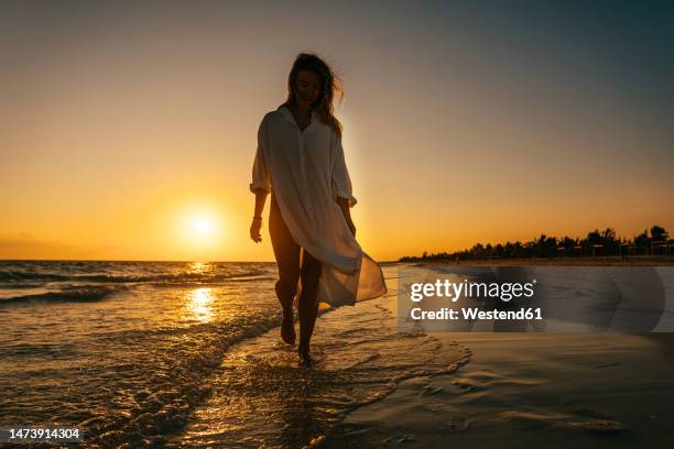 carefree woman strolling near shore on beach at sunrise - kuba strand stock-fotos und bilder