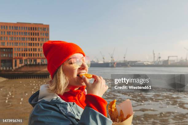 woman wearing sunglasses eating fish and chips - vertebrate stockfoto's en -beelden