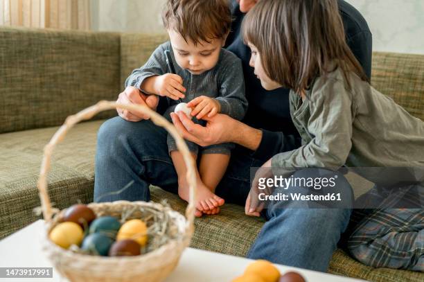 father and sons decorating eggs for easter at home - easter eggs basket stock-fotos und bilder