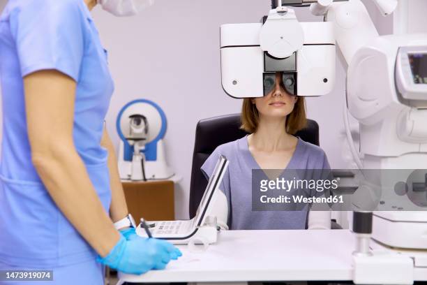 doctor with patient doing eyesight check up through phoropter at clinic - eye scanner stock pictures, royalty-free photos & images