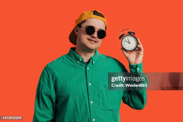 happy man standing with alarm clock against coral background - orange alarm clock stock pictures, royalty-free photos & images
