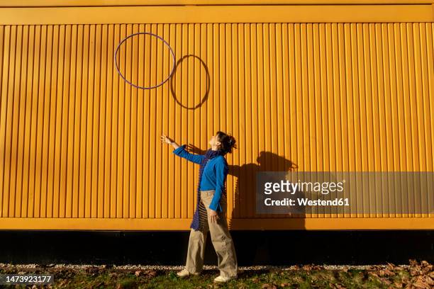 young woman tossing hula hoop near yellow container on sunny day - ring toss bildbanksfoton och bilder