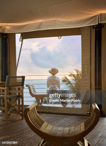mature female tourist admiring view at sunrise, while relaxing on decking of tented villa, at eco friendly luxury glamping resort. - eco tourism stock pictures, royalty-free photos & images