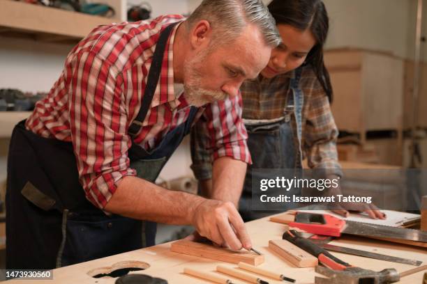 craftsman senior man teaching woman apprentice at woodshop, carpenter training wood for female standing at wood table in workshop, national carpenters day - national teacher stock pictures, royalty-free photos & images