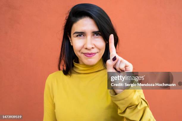 latino woman smiling, looking at the camera and giving the number one sign, medium shot - woman index finger stock pictures, royalty-free photos & images