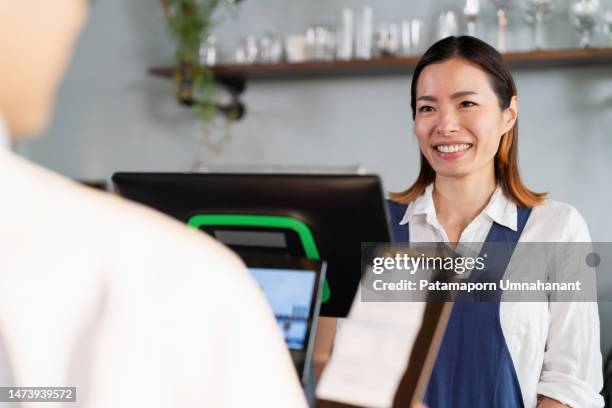 customer feedback improve business to growth continuously. japanese barista in apron standing in the cashier counter and give the customer bill with smile at the coffee shop. customer looking at the bill and make payment - coffee maker stock pictures, royalty-free photos & images