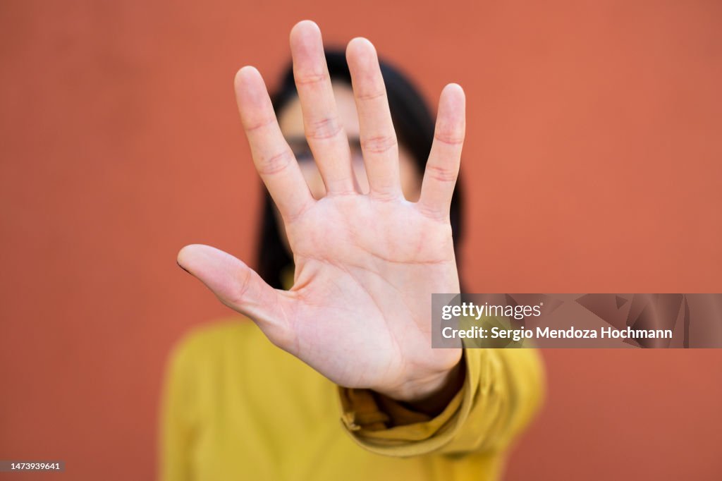 Latino woman looking at the camera and gesturing to STOP, close up, face obscured by hand