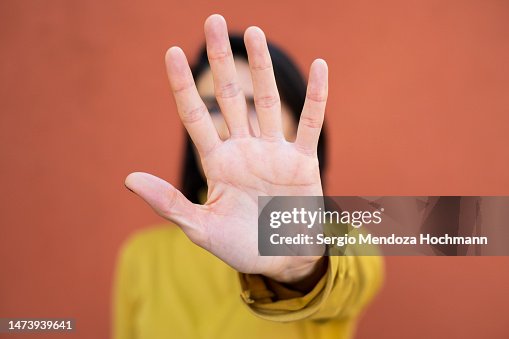 Latino woman looking at the camera and gesturing to STOP, close up, face obscured by hand Latino woman looking at the camera and gesturing to STOP, close up, face obscured by hand