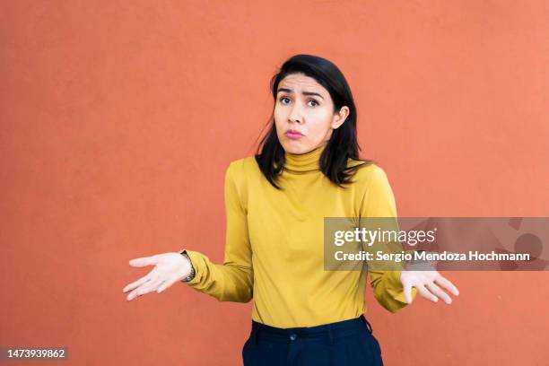 latino woman shrugging with her hands to the sides - confusione mentale foto e immagini stock